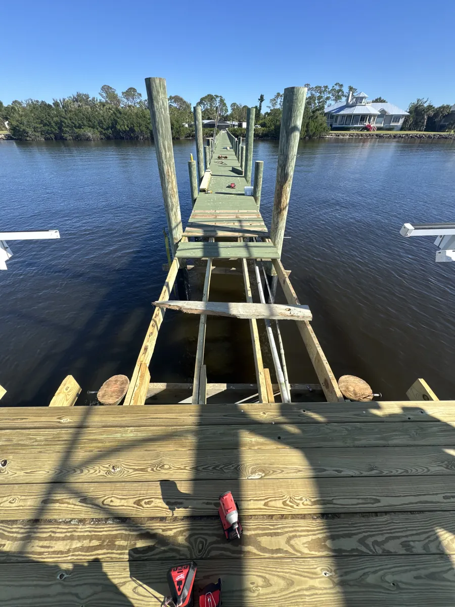 Exposed dock framing between timber decking and pilings over calm water.