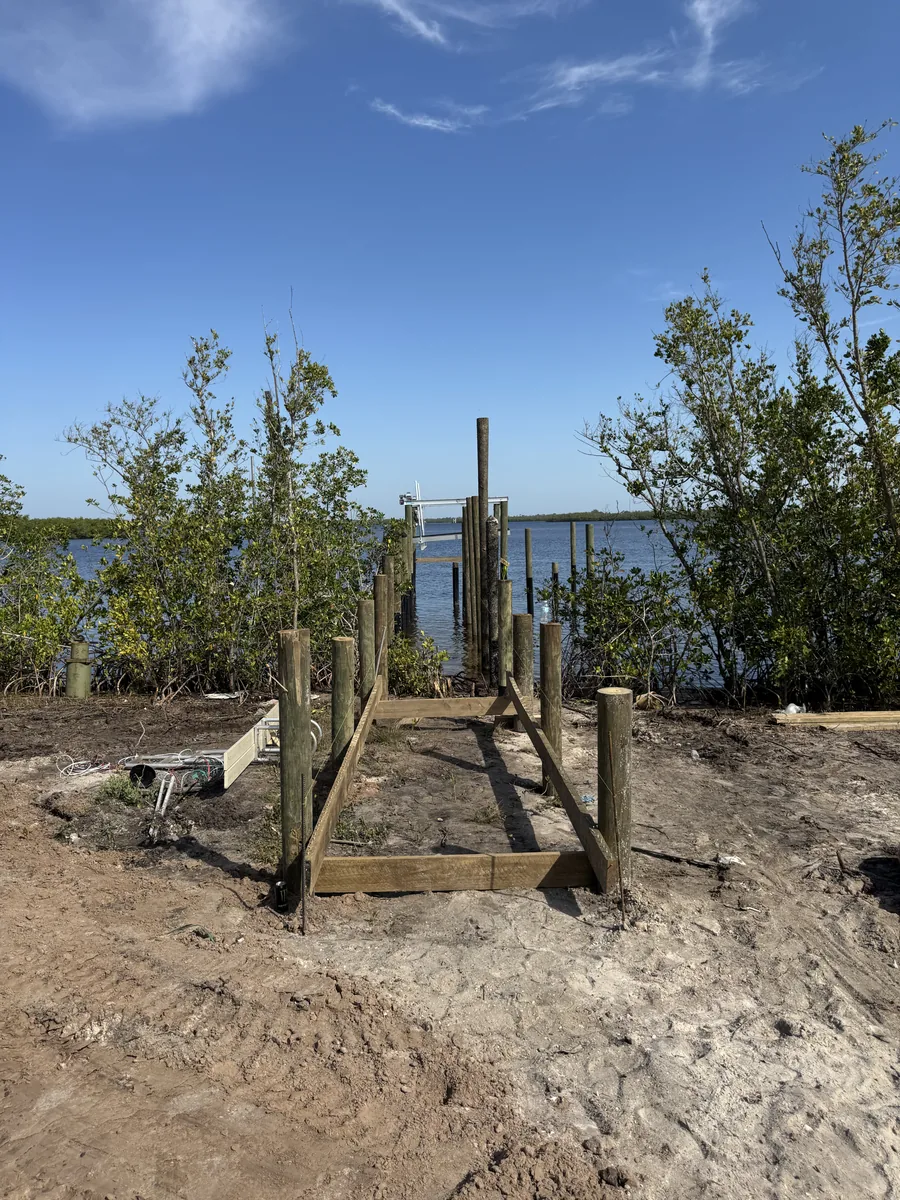 Timber dock framing and posts at a cleared shoreline leading toward open water
