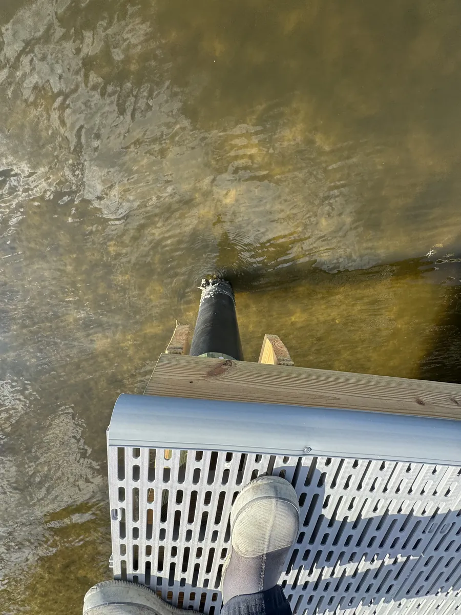 Close view of a grated dock edge and supporting structure over shallow water.