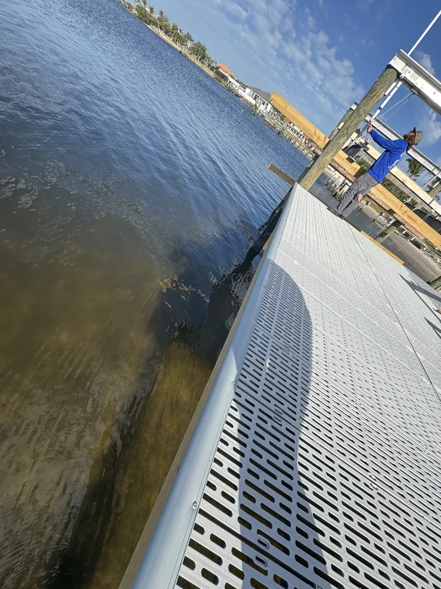 Angled view along a light gray grated dock surface and timber pilings beside water.