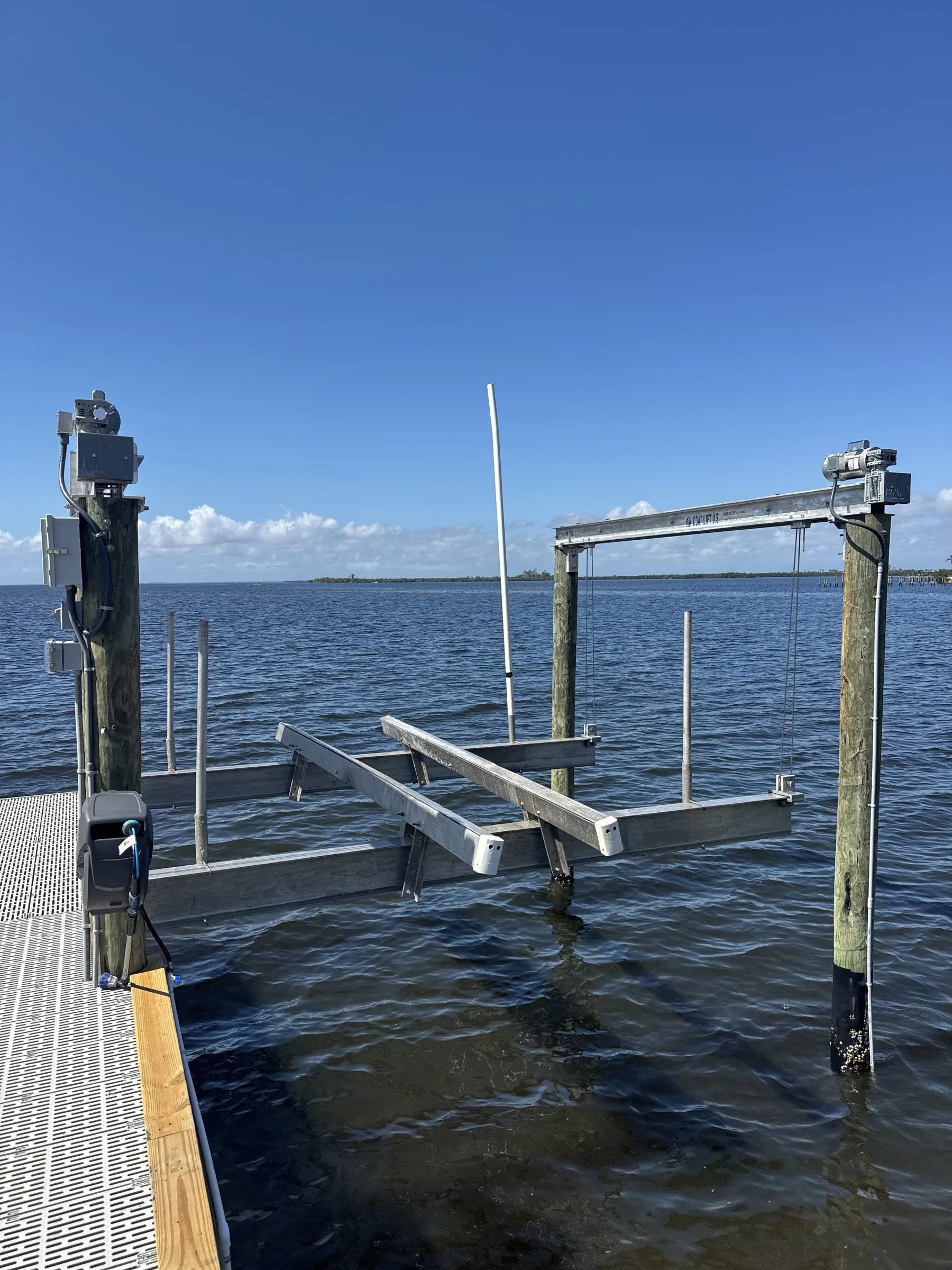 An aluminum boat lift and timber pilings beside blue open water