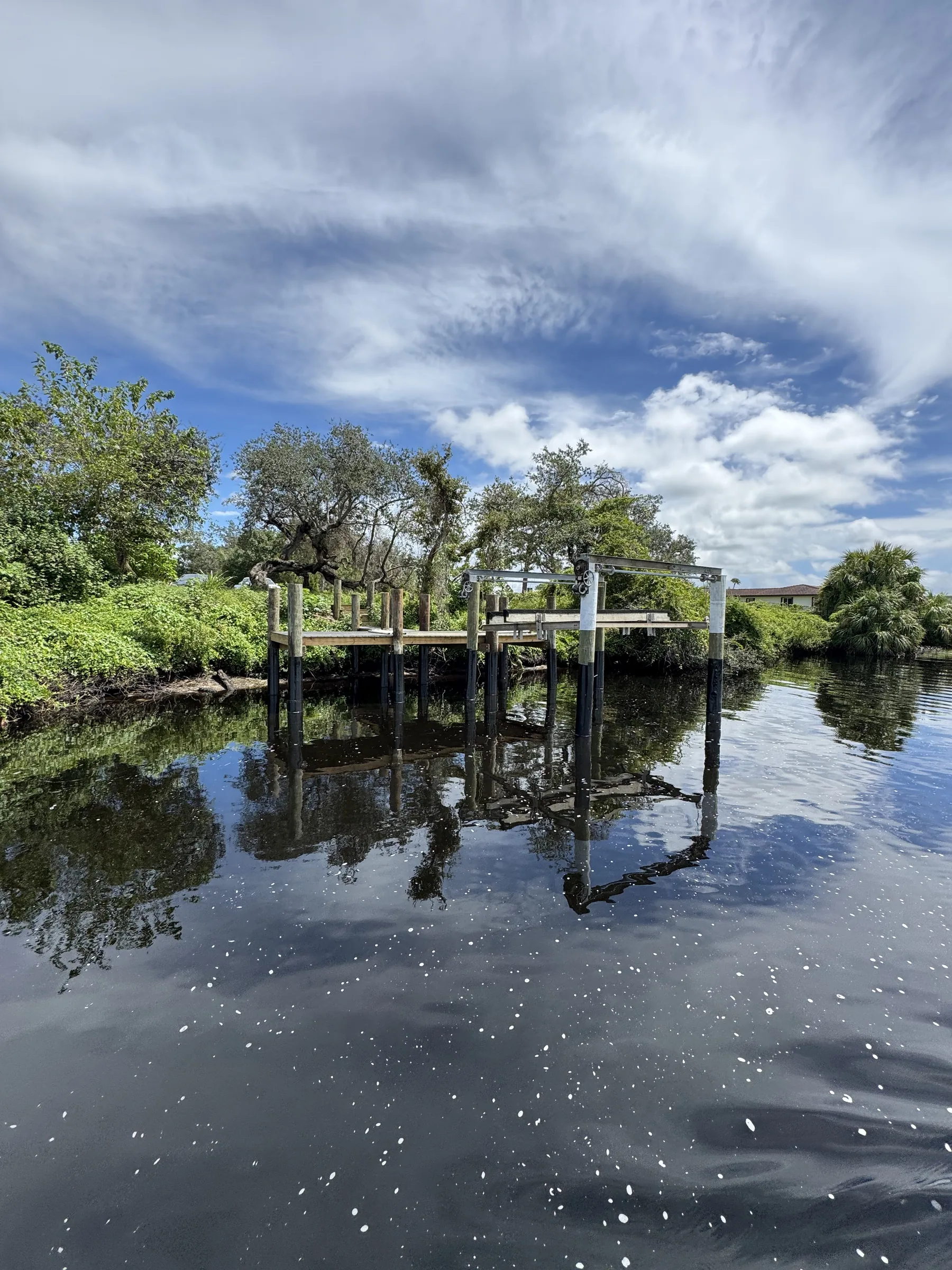 A boat lift and timber pilings reflected in calm water along a leafy shoreline