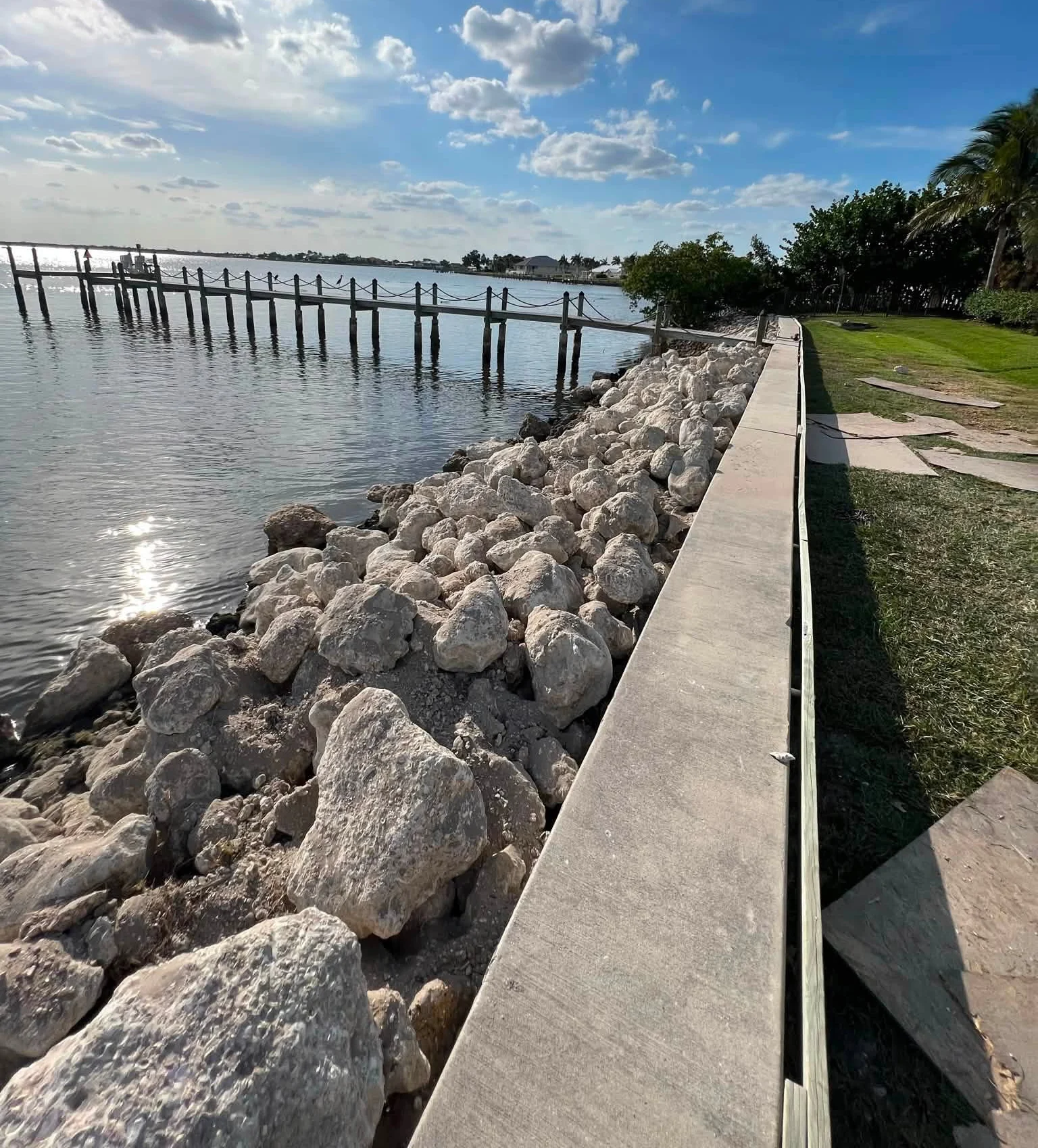 Riprap rocks along the water side of a seawall with a dock beyond