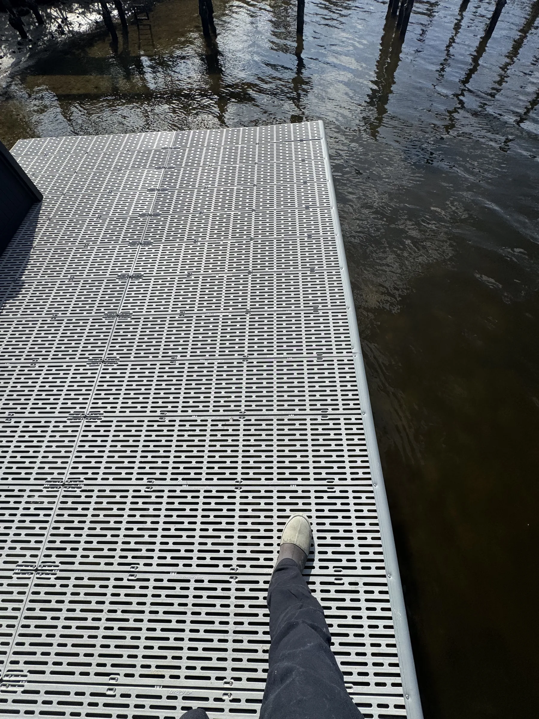 A close view of gray grated dock panels and fasteners beside the water