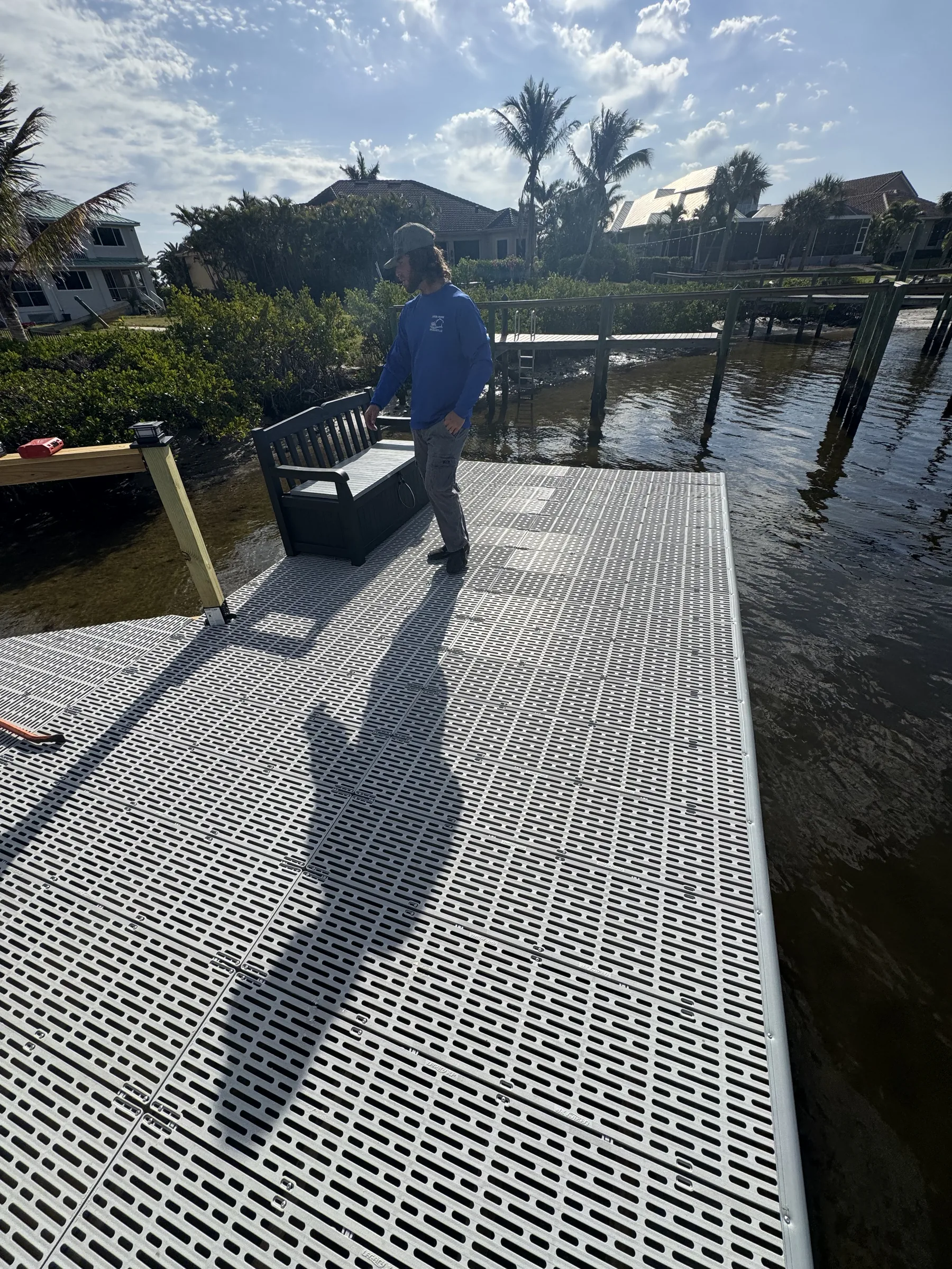A crew member standing beside a bench on a grated waterfront dock