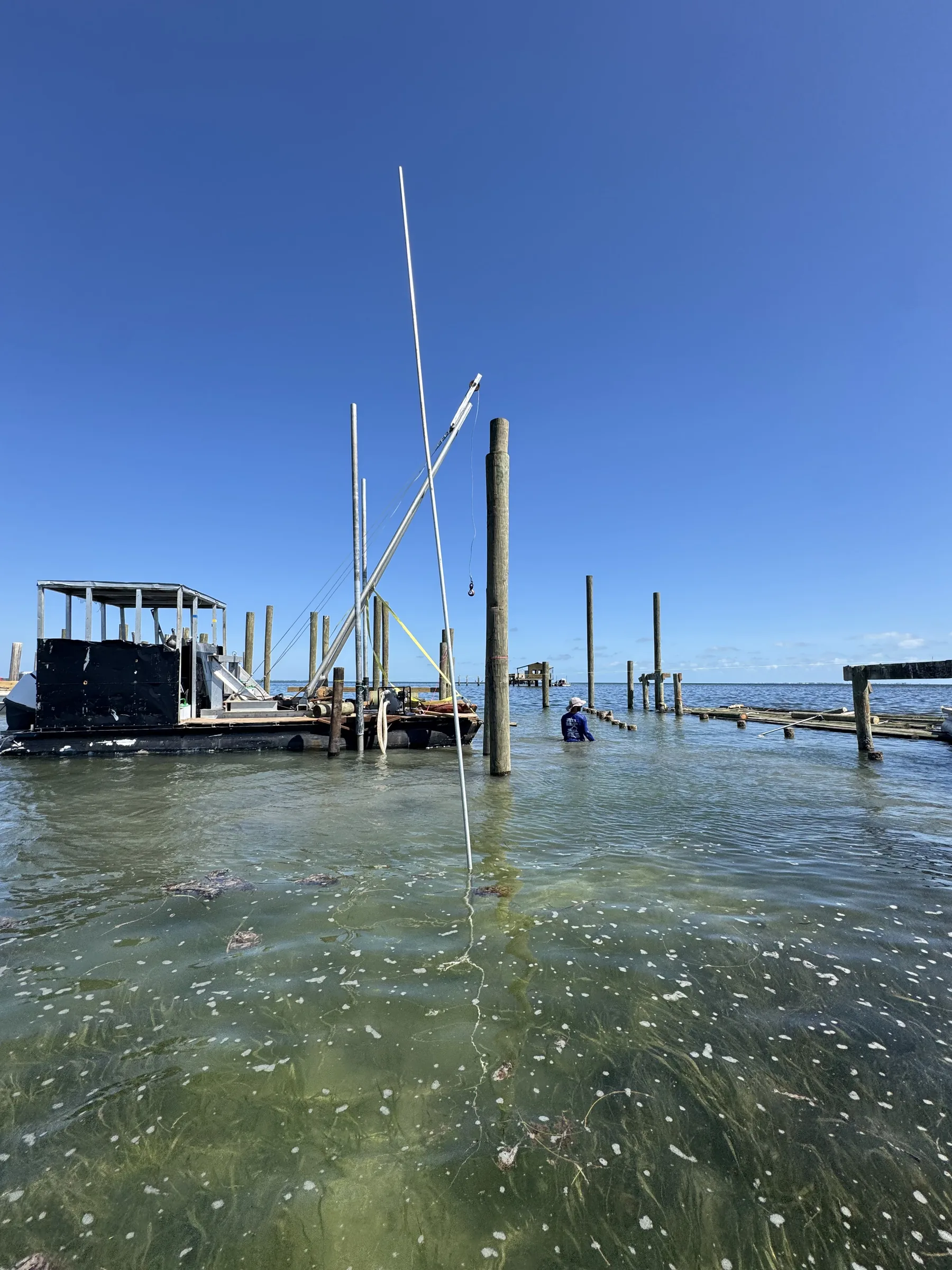 A marine work barge, crew member and timber pilings viewed from the water