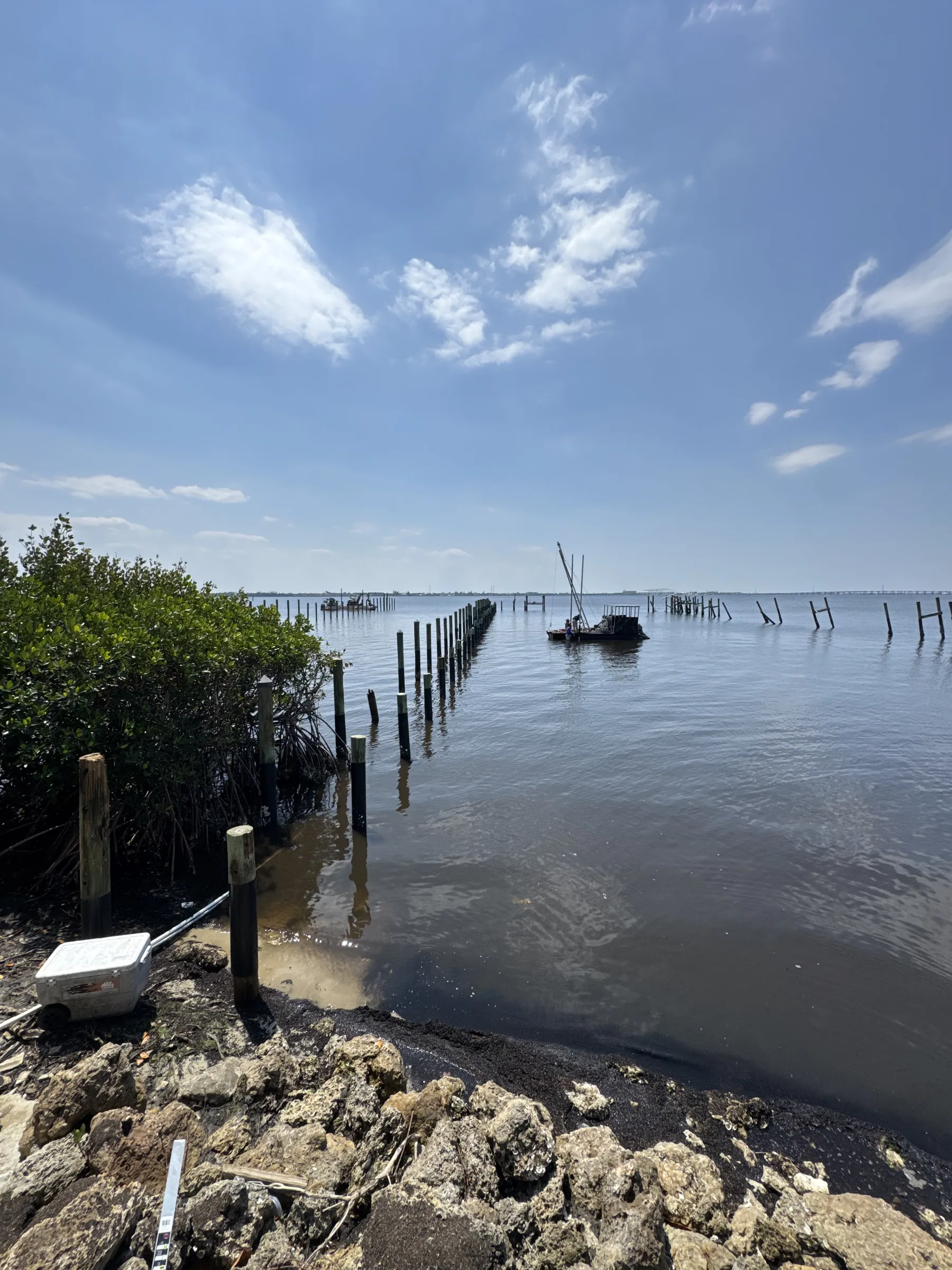 Timber pilings and a work vessel beyond a rocky shoreline