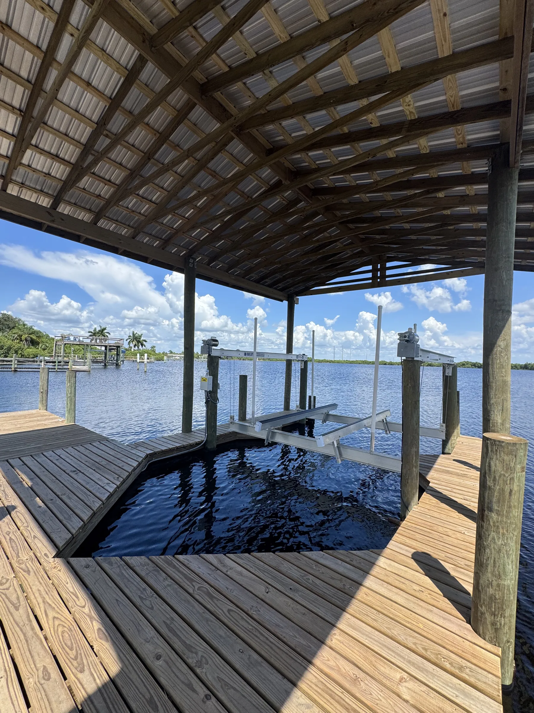 Covered timber dock with boat lift over blue water beside a Florida waterfront