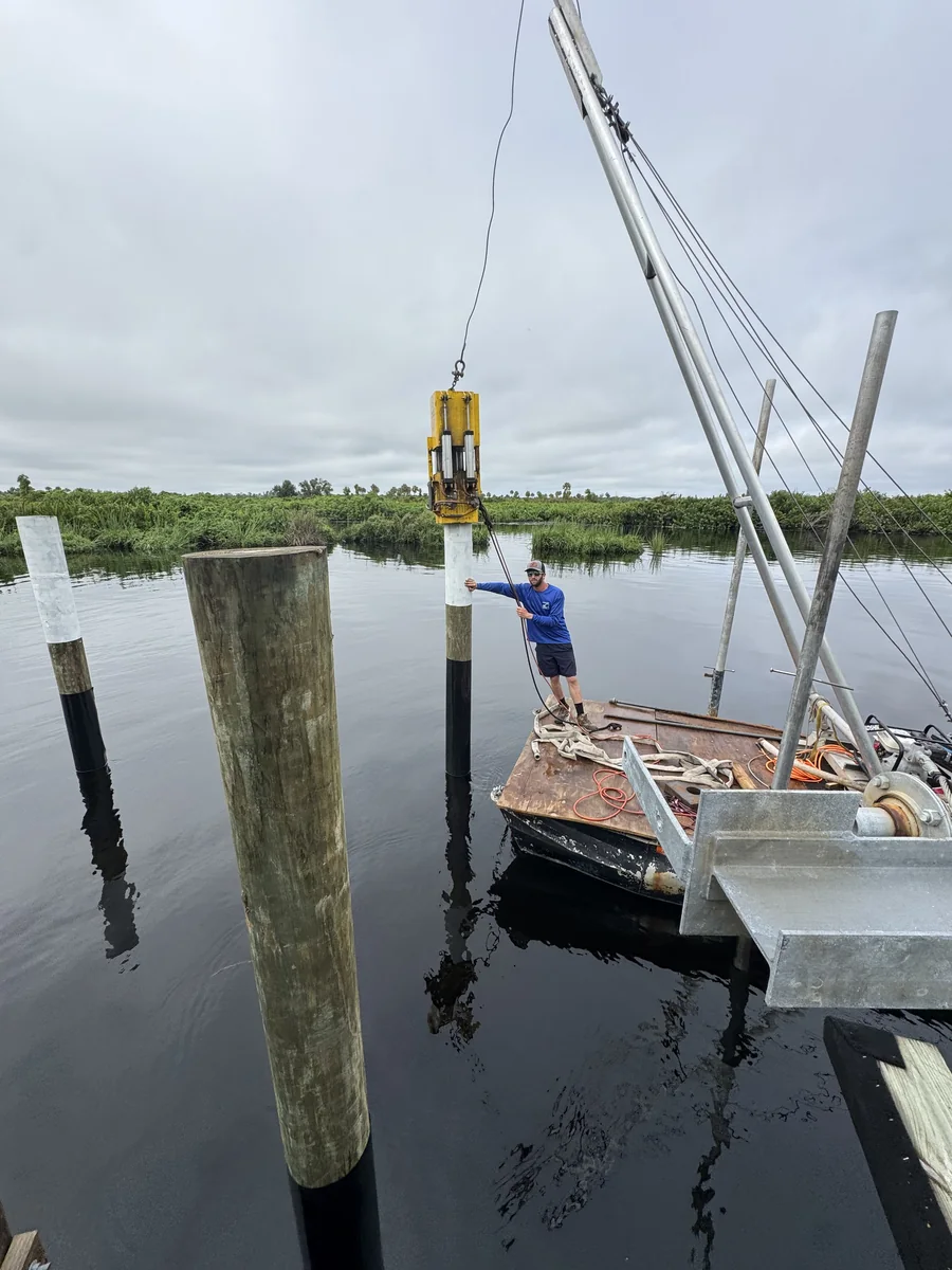 A crew member guiding a timber pile from a work barge